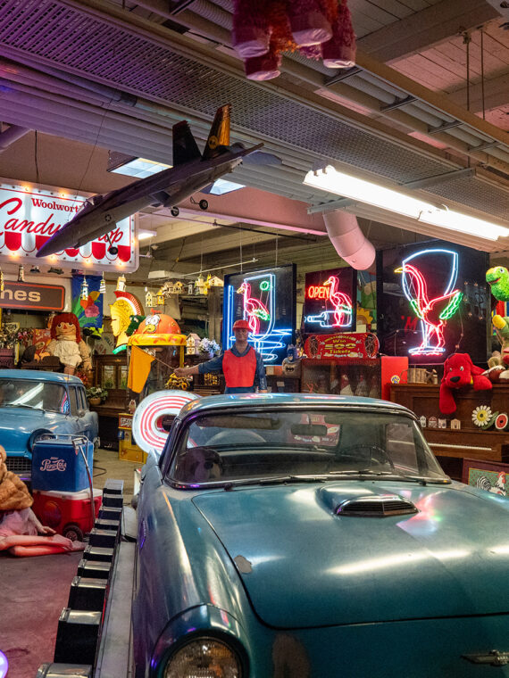 A vintage blue convertible is surrounded by colorful neon signs, toys, figures and other nostalgic memorabilia inside the American Treasure Tour Museum.