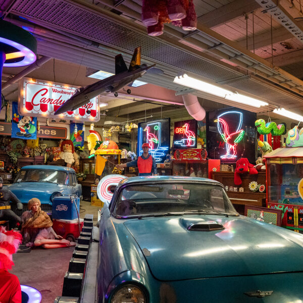 A vintage blue convertible is surrounded by colorful neon signs, toys, figures and other nostalgic memorabilia inside the American Treasure Tour Museum.