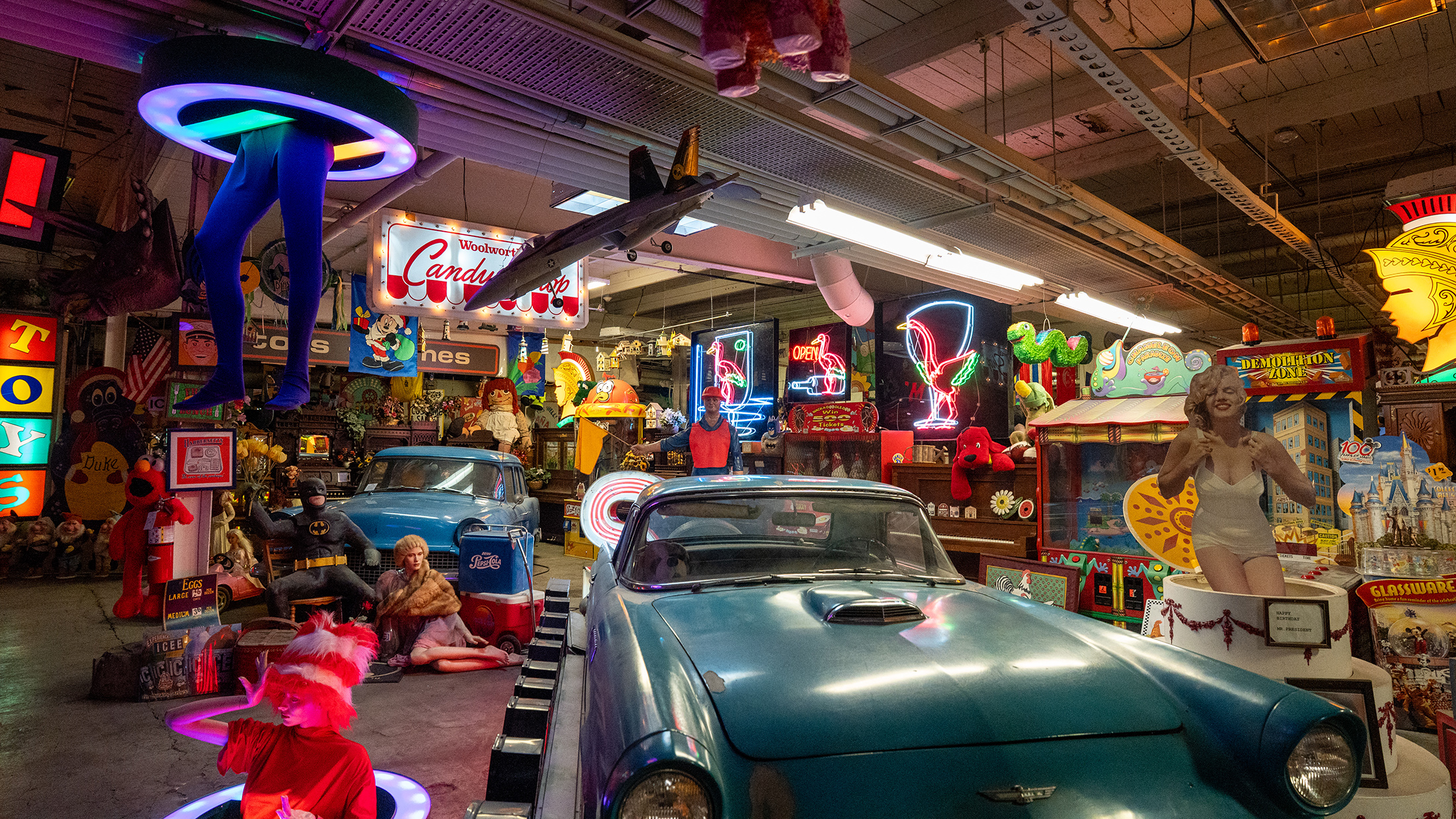 A vintage blue convertible is surrounded by colorful neon signs, toys, figures and other nostalgic memorabilia inside the American Treasure Tour Museum.