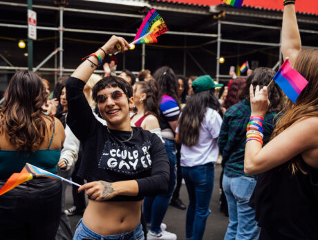 Uma pessoa dança alegremente com uma bandeira do arco-íris em cada mão em uma multidão de pessoas no OURFest na Filadélfia.