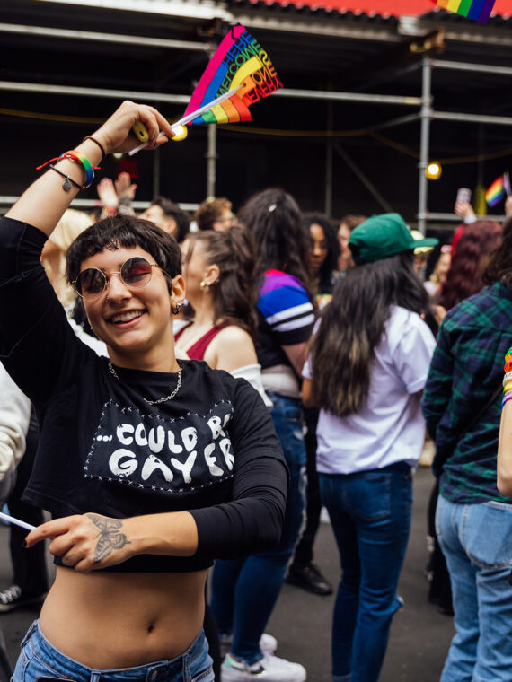 A person joyfully dances with a rainbow flag in each hand in a crowd of people at OURFest in Philadelphia.