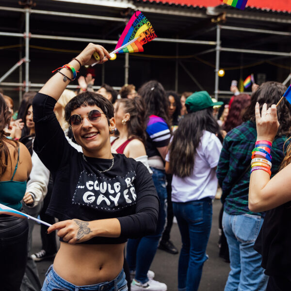 Una persona baila alegremente con una bandera arco iris en cada mano entre la multitud que asiste al OURFest de Filadelfia.
