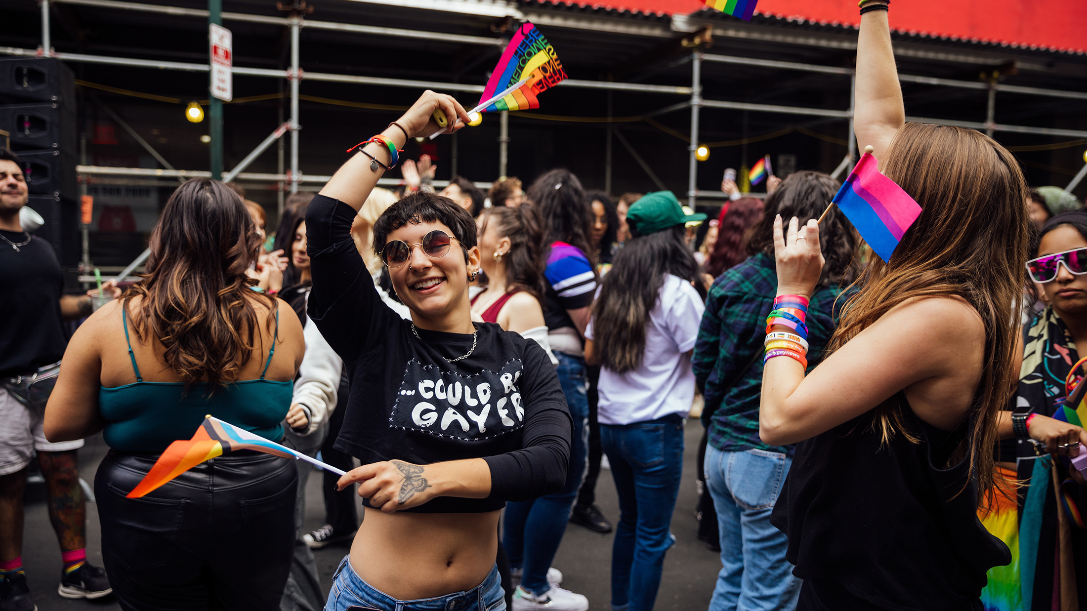 Una persona baila alegremente con una bandera arcoíris en cada mano entre una multitud de personas en el OURFest de Filadelfia.