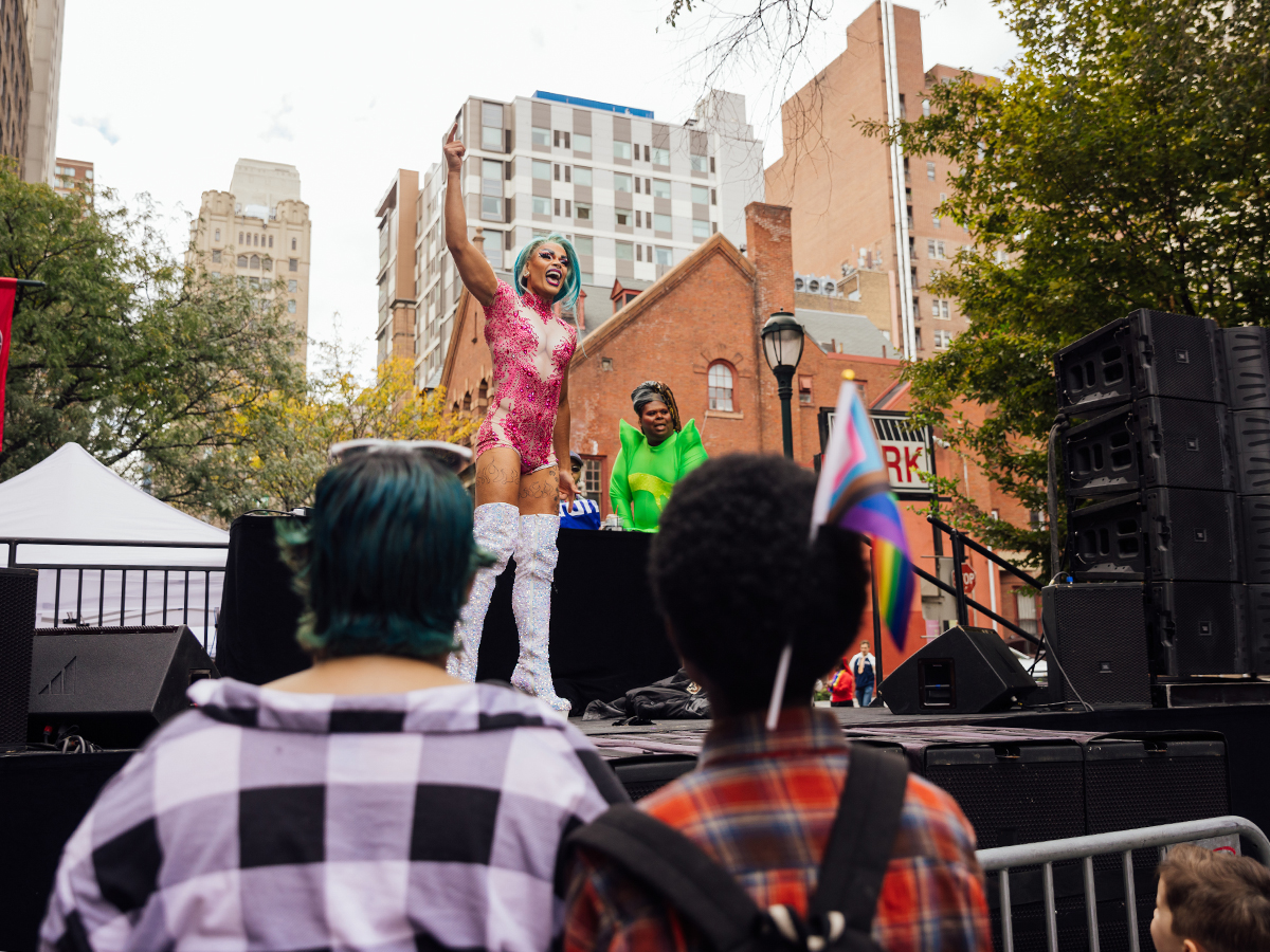 A drag performer in a bright pink outfit and knee-high sparkling silver boots performs onstage for a crowd at Ourfest.
