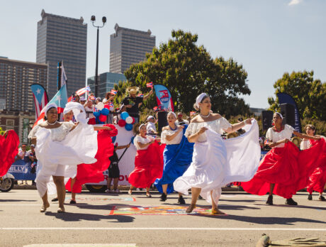 Dancers in flowing red, white and blue dresses perform in the Puerto Rican Day Parade on a car free street as spectators and parade participants gather behind them