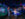 Two excited kids run hand-in-hand through a dark, blue-lit space exhibit filled with colorful interactive displays about planets and wavy LED lights.