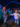 Two excited kids run hand-in-hand through a dark, blue-lit space exhibit filled with colorful interactive displays about planets and wavy LED lights.