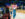 Une femme et un enfant, vêtus de tenues aux couleurs des 76ers de Philadelphie, marchent au bord du terrain à la Xfinity Mobile Arena tandis que les joueurs s'échauffent sur le terrain de basket.
