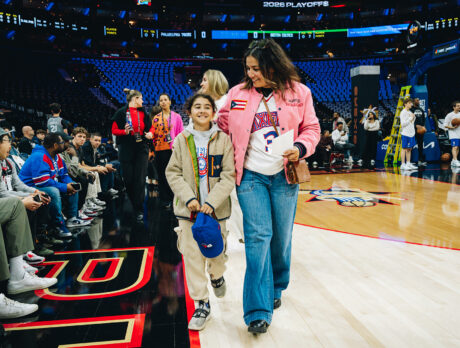Une femme et un enfant, vêtus de tenues aux couleurs des 76ers de Philadelphie, marchent au bord du terrain à la Xfinity Mobile Arena tandis que les joueurs s'échauffent sur le terrain de basket.