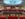 Un auditorio de teatro vacío con hileras de asientos rojos en los niveles de la platea y el balcón, bajo una gran estructura iluminada en el techo.