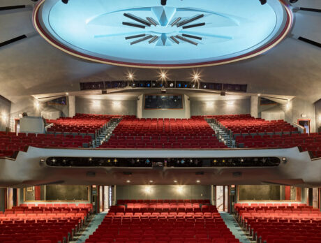 Un auditorio de teatro vacío con hileras de asientos rojos en los niveles de la platea y el balcón, bajo una gran estructura iluminada en el techo.