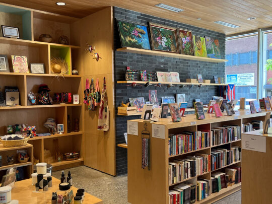 No interior da Livraria Julia de Burgos, no Taller Puertorriqueño. Os livros estão expostos nas prateleiras, com outros produtos ao redor