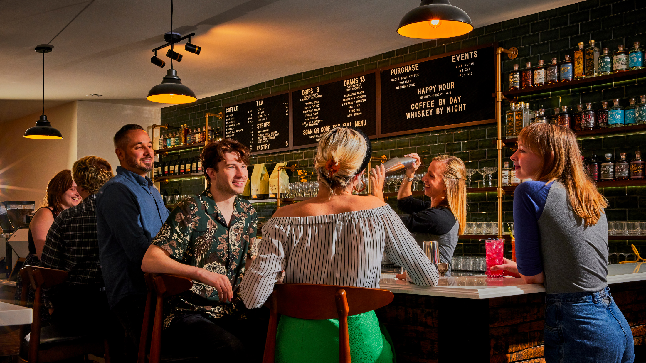 Um grupo de convidados conversa em um bar de coquetéis, onde um barman prepara um coquetel sob a luz aconchegante de luminárias pendentes e prateleiras repletas de bebidas destiladas.