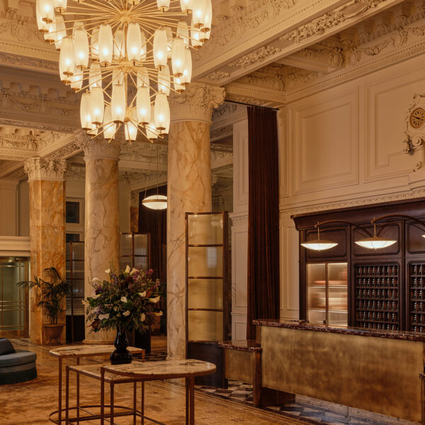 Le grandiose hall de l'hôtel Bellevue, avec ses détails architecturaux raffinés, ses colonnes en marbre, son comptoir d'accueil doré et ses lustres somptueux suspendus sous un plafond aux ornements complexes.