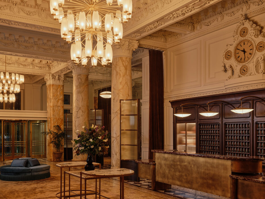 O imponente saguão do The Bellevue Hotel, com detalhes arquitetônicos ornamentados, colunas de mármore, um balcão de recepção dourado e lustres imponentes sob um teto ricamente decorado.