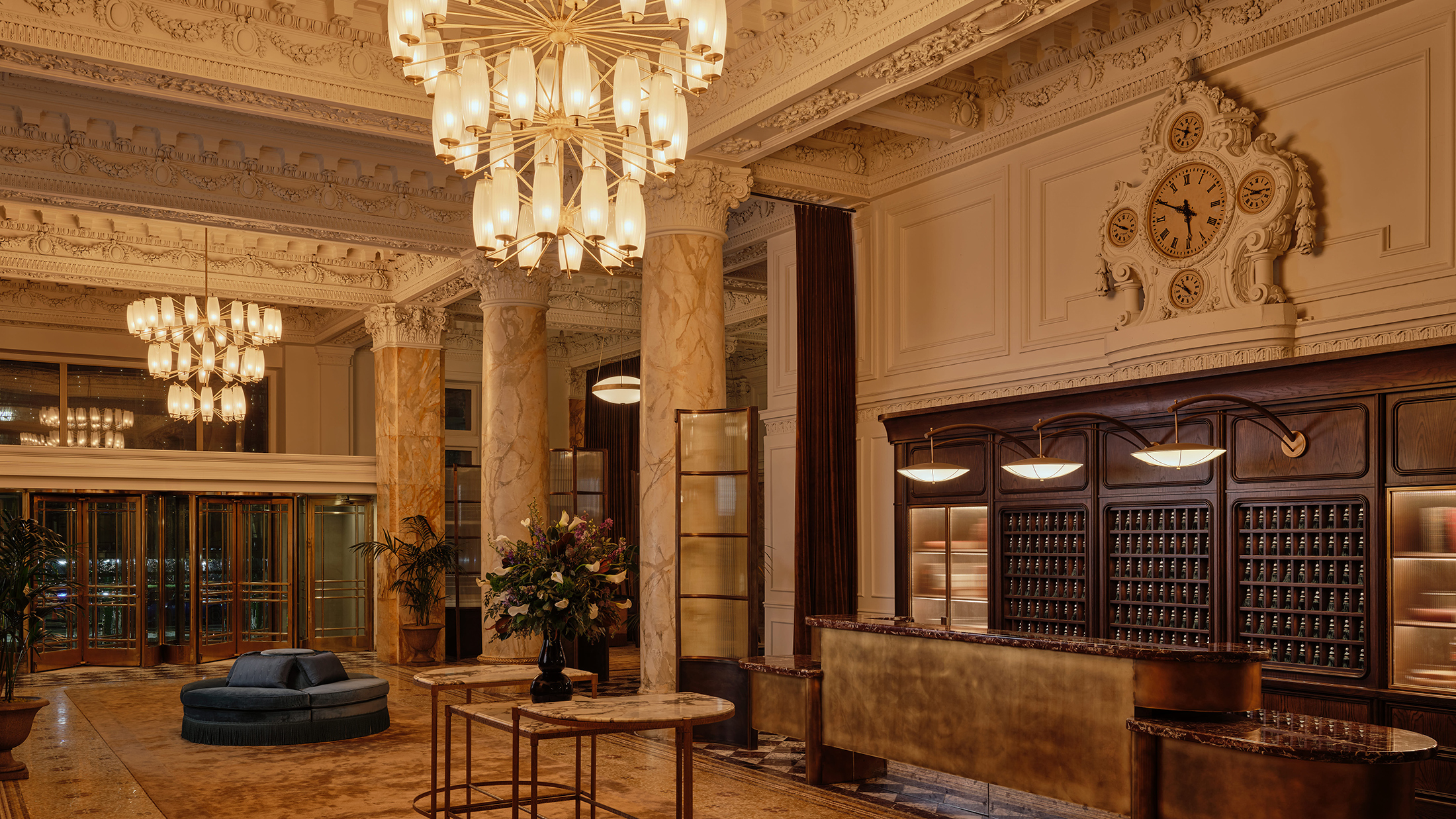O imponente saguão do The Bellevue Hotel, com detalhes arquitetônicos ornamentados, colunas de mármore, um balcão de recepção dourado e lustres imponentes sob um teto ricamente decorado.