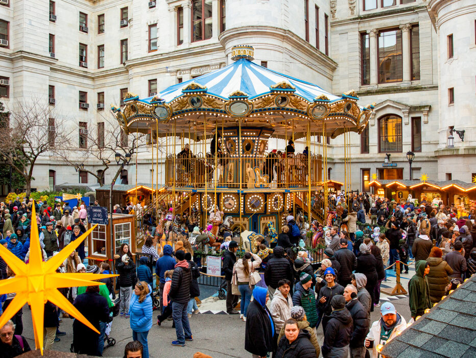 Visitors explore rows of wooden holiday market stalls decorated with glowing lights and star shaped ornaments, with a colorful Ferris wheel in the center.