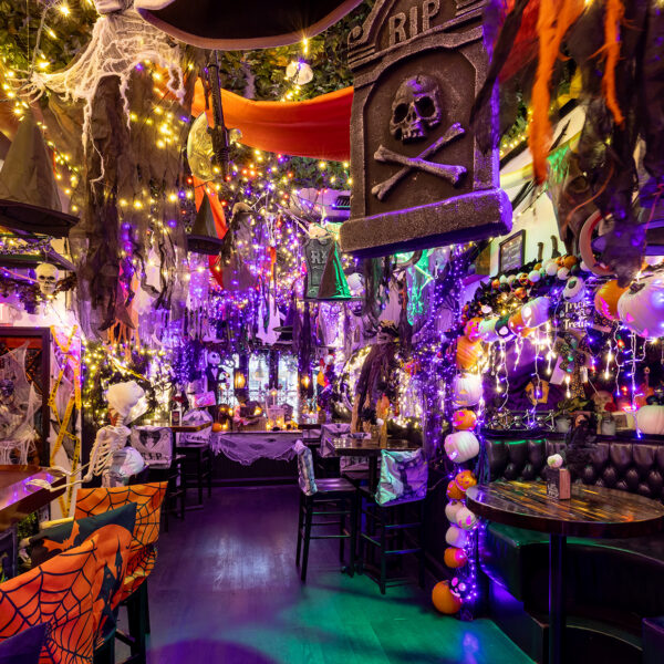 Au Craftsman Row Saloon, un bar est décoré de manière festive avec des guirlandes lumineuses violettes et orange, des chapeaux de sorcière suspendus, des toiles d’araignée, des squelettes, des citrouilles et d’autres éléments de décoration effrayants.