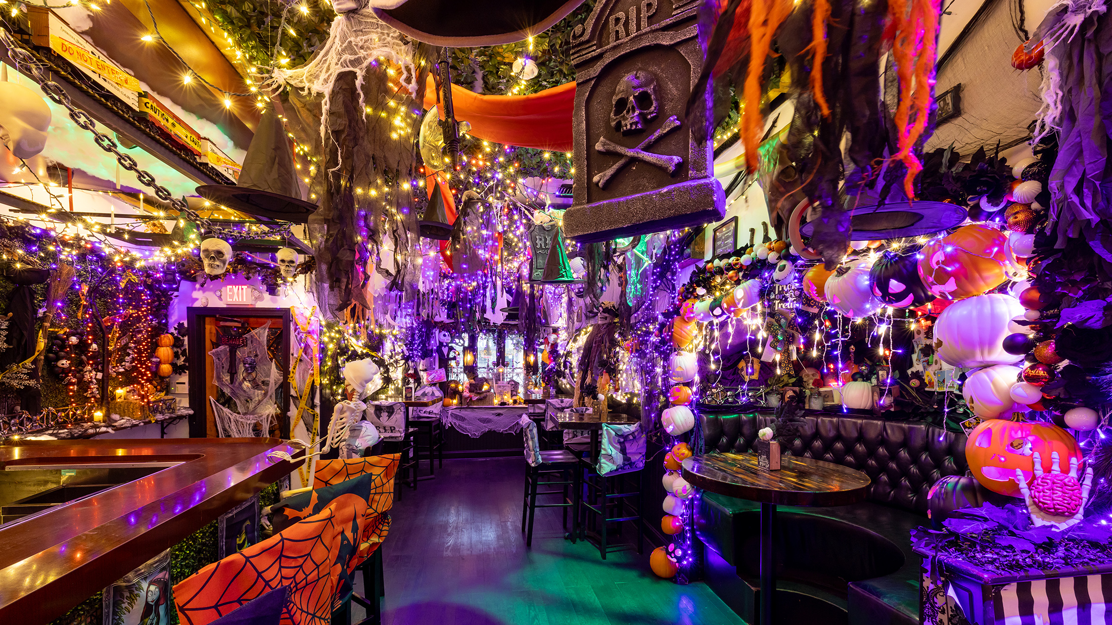 A bar is festively decorated with flowing purple and orange lights, hanging witches' hats, cobwebs, skeletons, pumpkins and other spooky decor at Craftsman Row Saloon.
