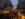 Crowds fill Christmas Village in Philadelphia at dusk, browsing illuminated wooden market stalls surrounding the iconic red LOVE sculpture and a glowing holiday pyramid.