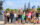 A large group of Rocky fans and tour participants raise their fists in a victory pose beside the Rocky statue, with the Philadelphia skyline visible behind them.