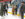 A group of adults and children dress in winter coats and hats smile together while wearing ice skates at an indoor ice rink.