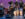 The Afro-Cuban All Stars perform on stage, featuring a lead vocalist playing guitar alongside musicians on piano, upright bass, percussion and brass instruments against a purple stage background.