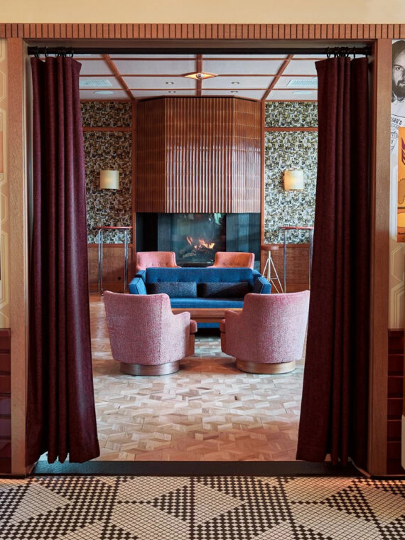 A retro-inspired lounge featuring walls covered in vintage concert posters, large speakers, patterned tile floors and a cozy seating area with pink chairs, a blue sofa and fireplace.
