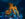 A glowing orange octopus sculpture made from carved pumpkins stretches its tentacle across a coral-covered rock formation inside a dark blue aquarium tank as fish swim nearby.