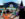 Two children wearing Halloween costumes, one wearing a pair of orange butterfly wings and the other in a purple-and-black witch outfit, walk hand-in-hand toward the decorated entrance of Sesame Place.