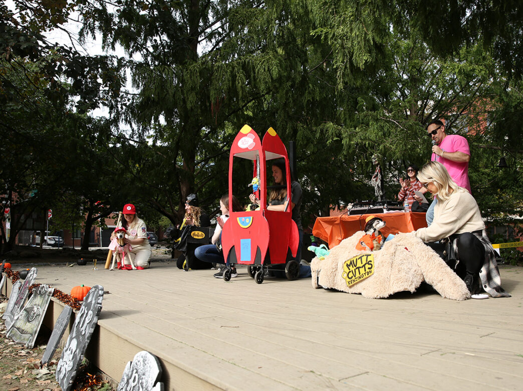 Costumed dogs and their owners patriciate in a Halloween-themed event, featuring festive decorations, creative pet costumes and a stage presentation.
