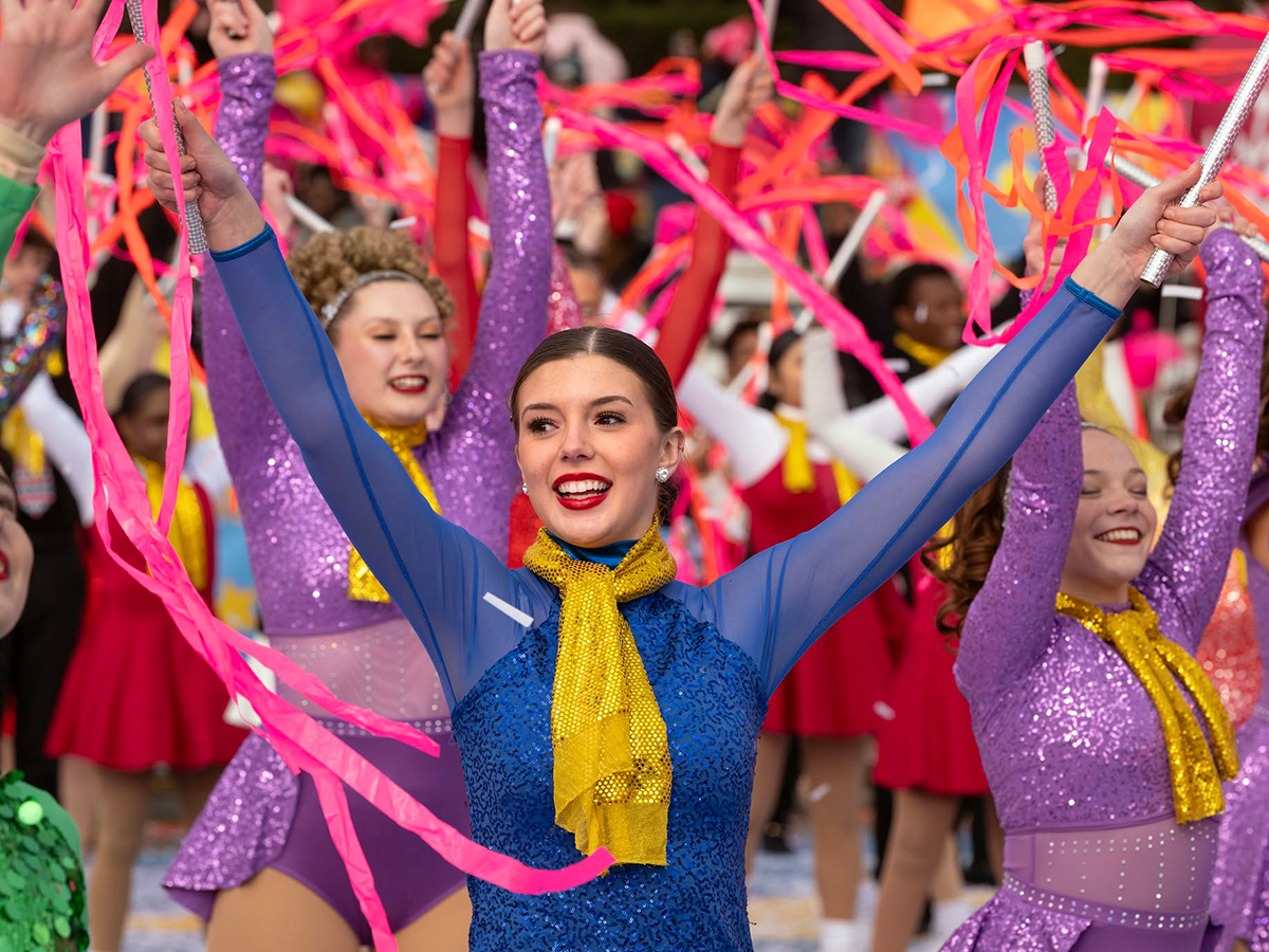 Dancers dressed in colorful blue and purple costumes with gold scarves wave bright pink and orange streamers during Philadelphia's 6abc Dunkin' Thanksgiving Day Parade.