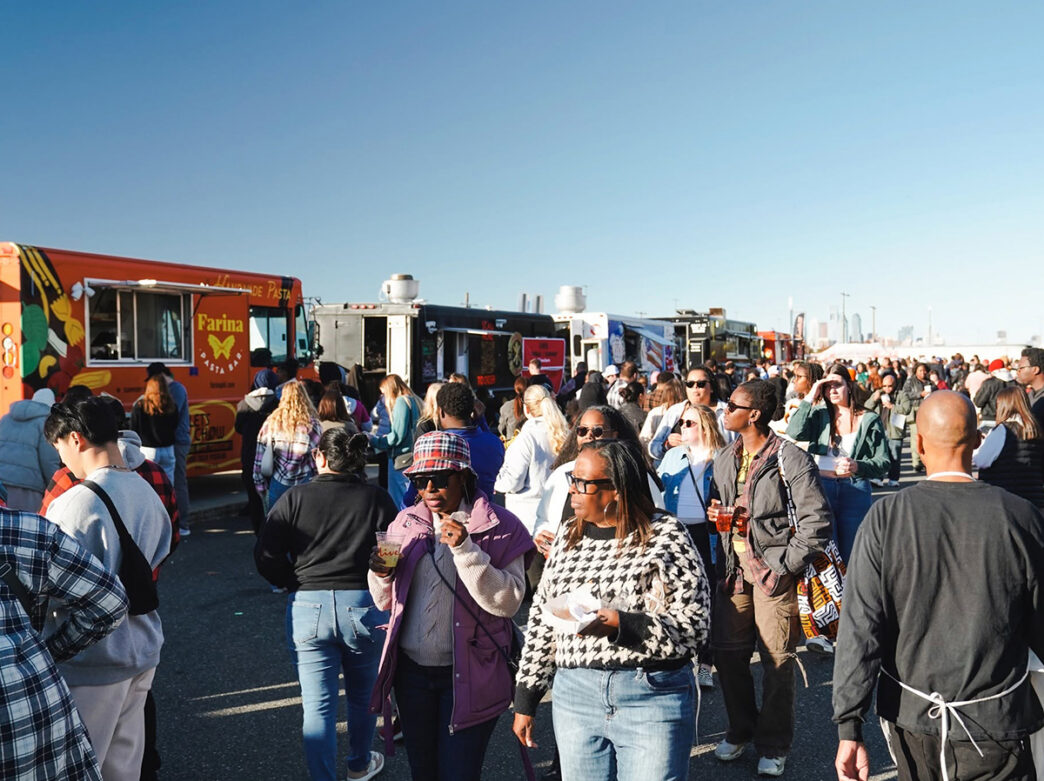 Los visitantes recorren un animado festival de comida callejera al aire libre, disfrutando de la comida y las bebidas que ofrecen diversos camiones de comida en un día soleado.